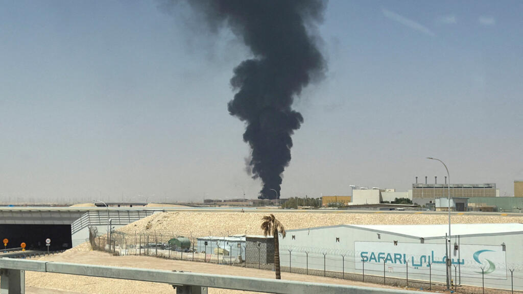 Thick black smoke billows into the sky from an industrial area in the desert.