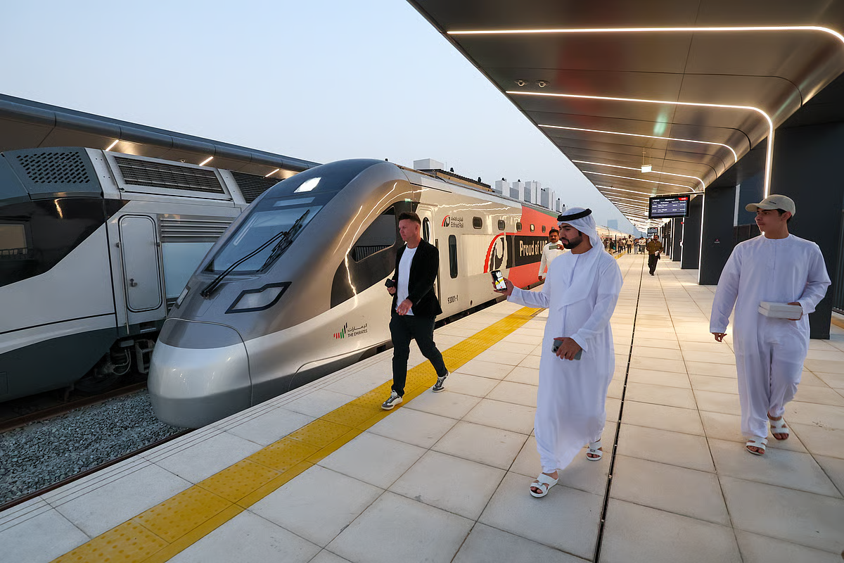 Commuters stand on the platform of a modern railway station next to a sleek Etihad Rail train in the UAE.